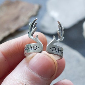 May include: Silver adjustable ring with a deer antler design. The ring has a band with a repeating pattern of symbols.