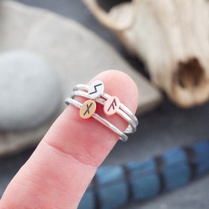 Peut inclure: Trois bagues empilables en argent avec de petits pendentifs ovales. Les pendentifs sont gravés de runes différentes.