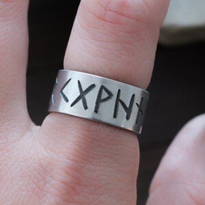 May include: A silver ring with the inscription "<XPNT" in black lettering.