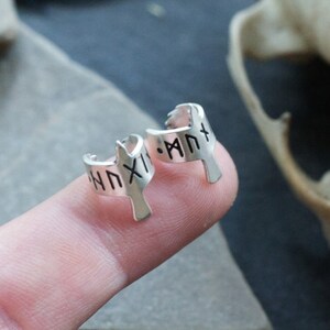 May include: A pair of silver hoop earrings with a bird design. The earrings are engraved with runes.