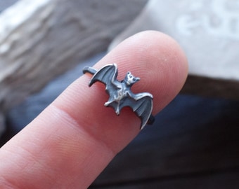 May include: A silver ring with a bat design. The bat is facing forward with its wings spread out.