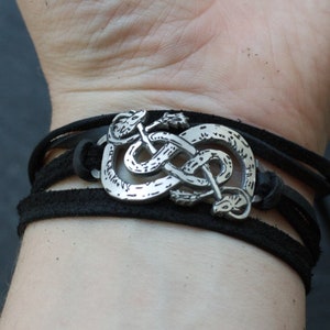 May include: A black leather bracelet with a silver snake knot charm. The bracelet is adjustable and has a braided leather design.