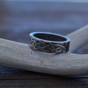 May include: A silver ring with a Celtic knot design sits on a white antler.