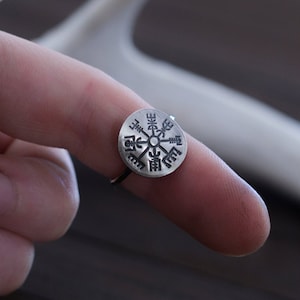 May include: A silver ring with a compass design featuring a Vegvisir symbol, a Norse directional symbol, engraved on the face.