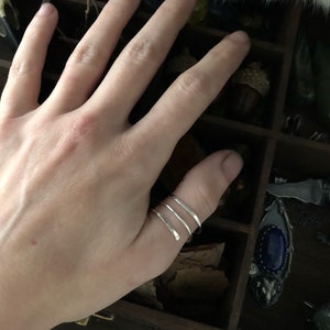 May include: A silver ring with three thin bands wrapped around the thumb.