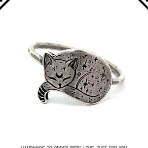 May include: A silver ring with a sleeping cat design. The cat is engraved with stars and a crescent moon. The ring is handmade to order.