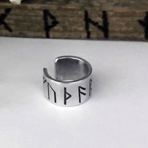 May include: Silver ring with a band of runes engraved in black. The runes are in a circular pattern.