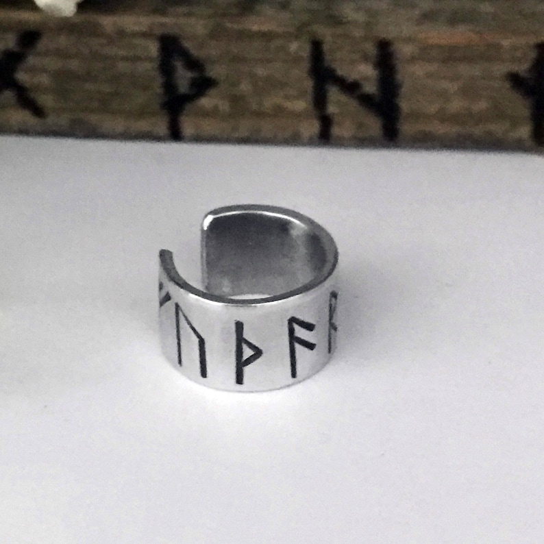 May include: Silver ring with a band of runes engraved in black. The runes are in a circular pattern.