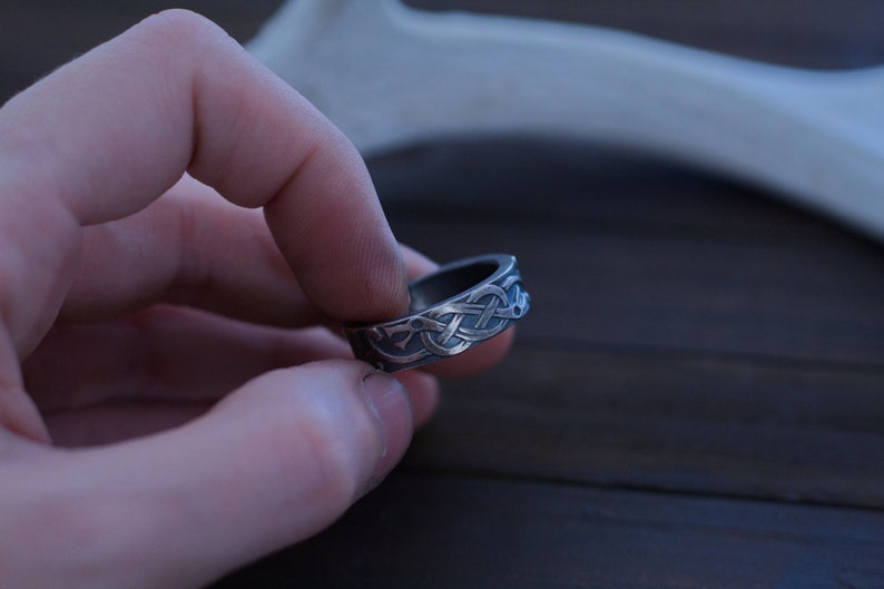 May include: A silver ring with a Celtic knot design. The ring is worn on a finger.