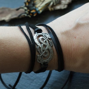 May include: A black leather wrap bracelet with a silver metal charm featuring a Celtic knot design.