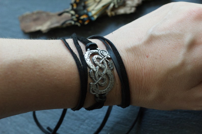 May include: A black leather wrap bracelet with a silver metal charm featuring a Celtic knot design.