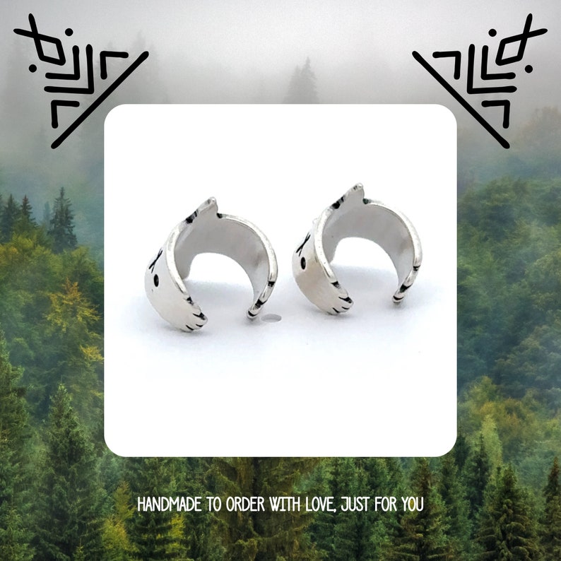 May include: A pair of silver ear cuffs with a geometric design. The cuffs are open and have a smooth, polished finish.