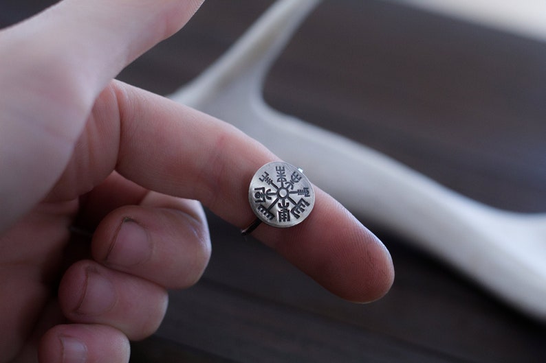 May include: A silver ring with a compass design featuring a Vegvisir symbol, a Norse directional symbol, engraved on the face.