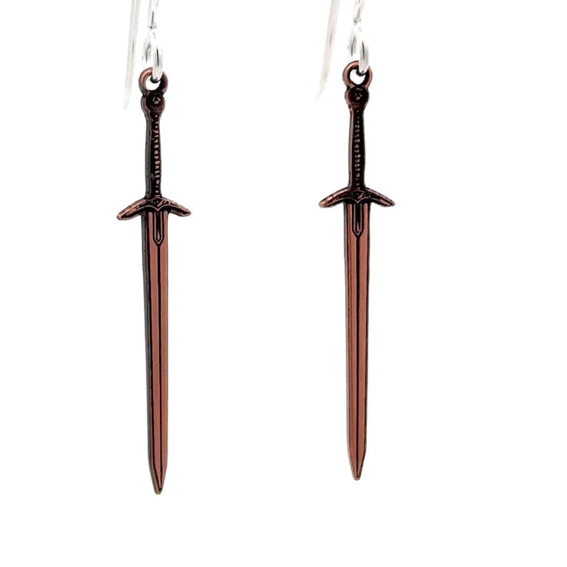 Peut inclure: Une paire de boucles d'oreilles pendantes argent&eacute;es avec un charme d'&eacute;p&eacute;e en cuivre. Les &eacute;p&eacute;es sont d&eacute;taill&eacute;es avec une garde crois&eacute;e et une pointe pointue.