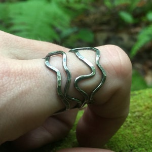 May include: Three silver rings stacked on a finger. The rings are made of wavy, hammered metal.