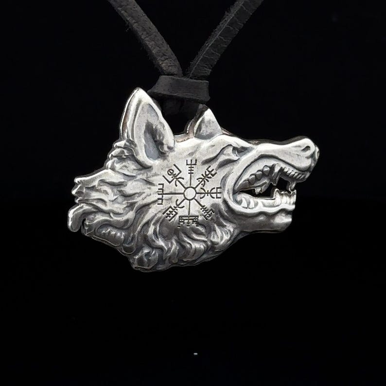 May include: Silver wolf head pendant necklace with a compass design featuring Norse runes. The pendant is on a black leather cord.