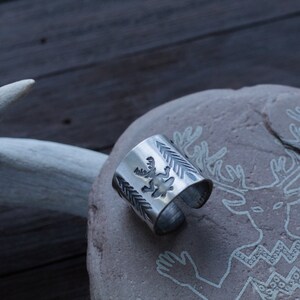 May include: A silver ring with a deer design on a stone background with a deer carving.