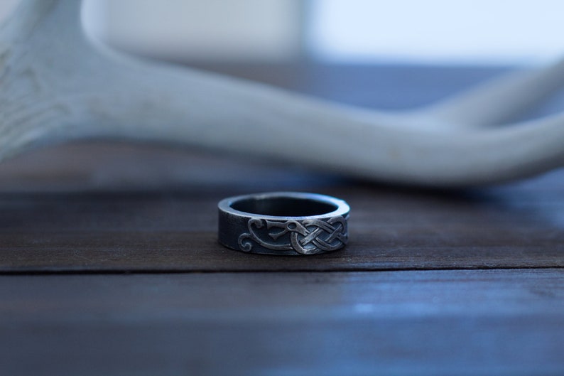 May include: A silver ring with a Celtic knot design. The ring is on a wooden surface.