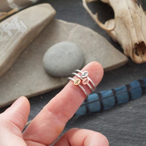 May include: Three silver rings with different rune symbols on the top of each ring. The rings are stacked on a finger.