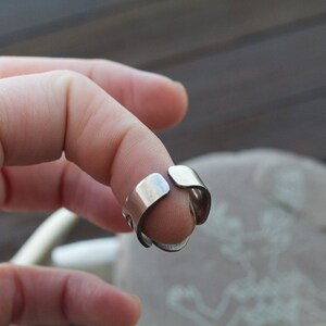 May include: A silver adjustable ring with a simple design. The ring is open on one side and can be adjusted to fit different finger sizes.