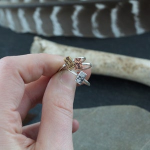 May include: Three silver rings with different colored rectangular stones. The stones are gold, copper, and silver.