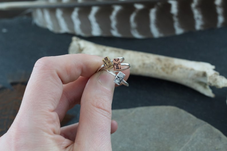 May include: Three silver rings with different colored rectangular stones. The stones are gold, copper, and silver.