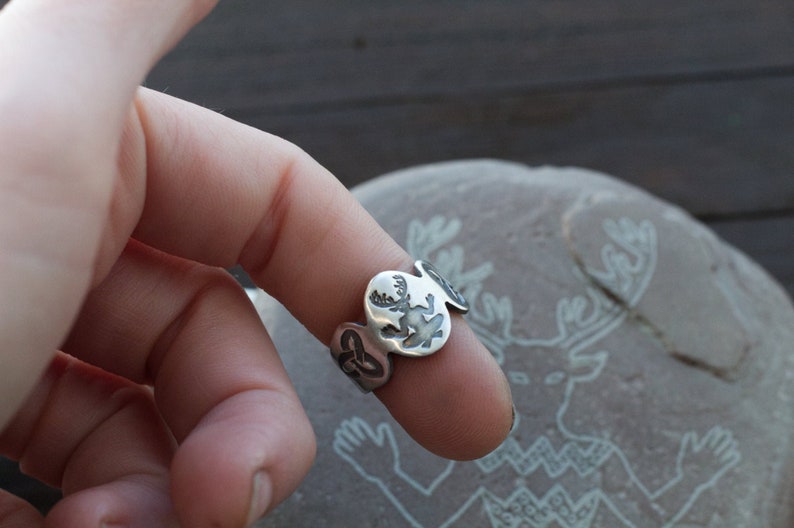 May include: A silver ring with a design of a deer with antlers. The ring is worn on a finger.