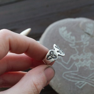 May include: A silver ring with a Celtic knot design and a stylized deer head. The ring is worn on a finger.