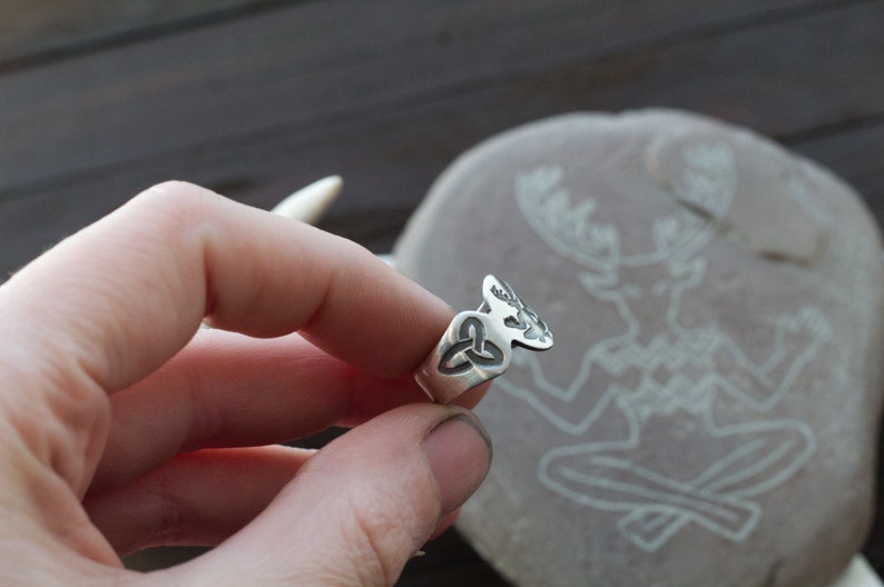May include: A silver ring with a Celtic knot design and a stylized deer head. The ring is worn on a finger.