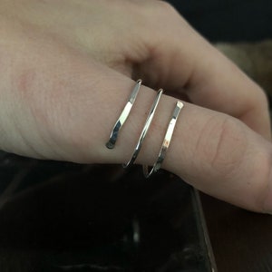 May include: Three silver rings stacked on a finger. The rings are thin and have a hammered texture.