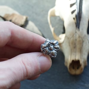 May include: A silver ring featuring a detailed flower design. The flower has a face in the centre.