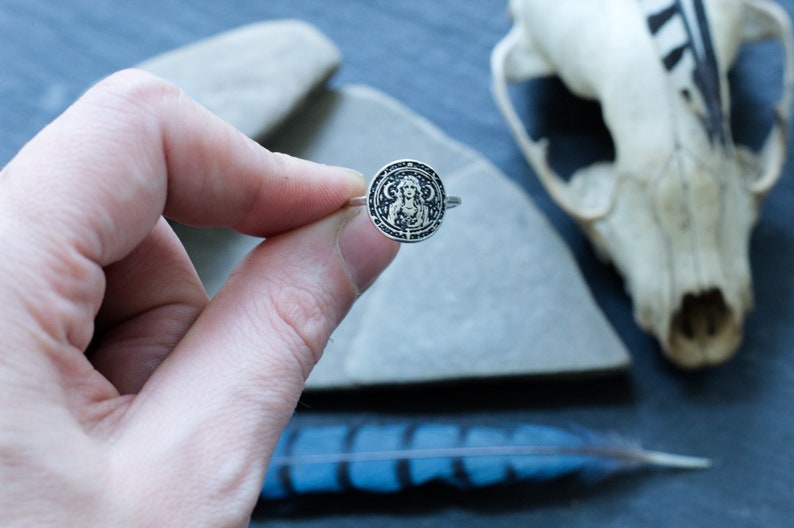 May include: A silver ring with a circular design featuring a woman's face and intricate details.