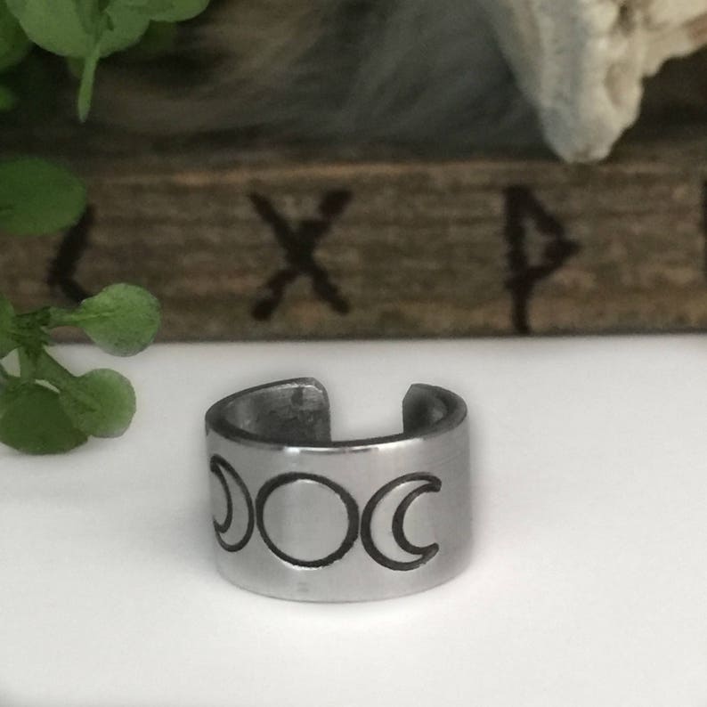May include: A silver ring with a triple moon design. The ring is made of metal and has a smooth finish.