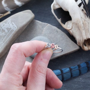 May include: Three silver rings with different runes engraved on them. The rings are stacked on top of each other and are being held by a hand.