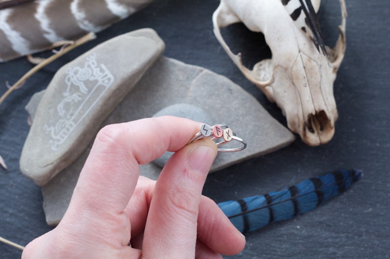 May include: Three silver rings with different runes engraved on them. The rings are stacked on top of each other and are being held by a hand.