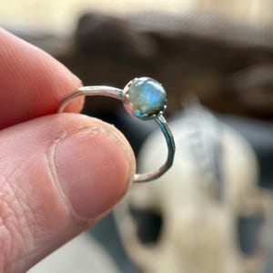 K&ouml;nnte beinhalten: Ein silberner Ring mit einem blaugr&uuml;nen Edelstein, der in einer Zargenfassung sitzt.