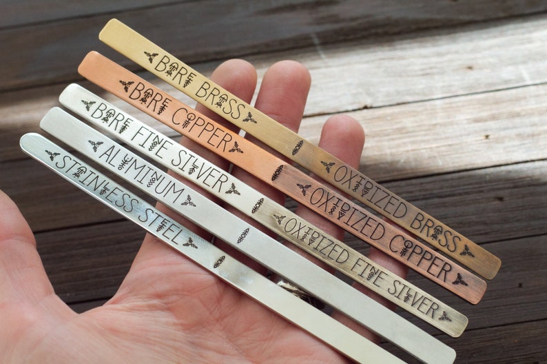 May include: Close-up of six metal strips, each labeled with a different metal type: Bare Brass, Bare Copper, Bare Fine Silver, Aluminum, Stainless Steel, Oxidized Fine Silver, Oxidized Copper, and Oxidized Brass.