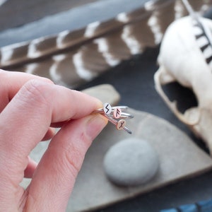 May include: A set of four silver rings with different runes engraved on them. The rings are stacked on top of each other and are being held by a hand.