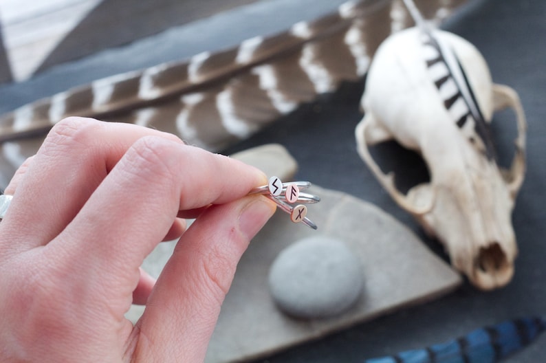 May include: A set of four silver rings with different runes engraved on them. The rings are stacked on top of each other and are being held by a hand.