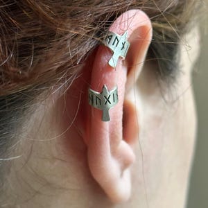 May include: A pair of silver ear cuffs in the shape of a bird with the inscription "HXIX" on each cuff.