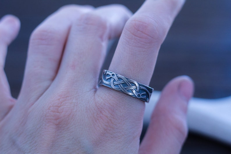 May include: A silver ring with a Celtic knot design. The ring is worn on a finger.