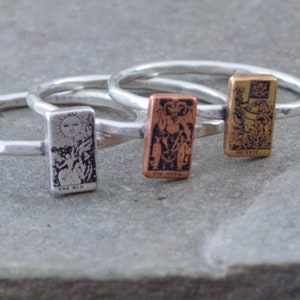 May include: Three silver rings with tarot card designs. The rings feature the Sun, Death, and the Lovers cards.