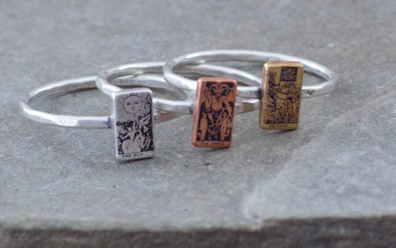 May include: Three silver rings with tarot card designs. The rings feature the Sun, Death, and the Lovers cards.