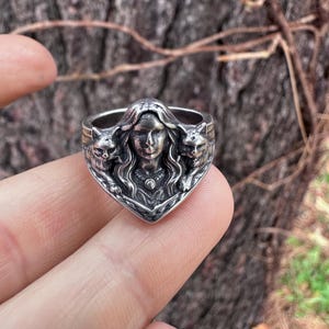 K&ouml;nnte beinhalten: Ein silberner Ring mit einer zentralen weiblichen Figur, flankiert von zwei Katzenfiguren. Der Ring hat aufwendige Details und einen Vintage-Look, ideal f&uuml;r Liebhaber von einzigartigem Schmuck.