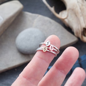 May include: Three silver rings with different runes engraved on them. The rings are stacked on a finger.
