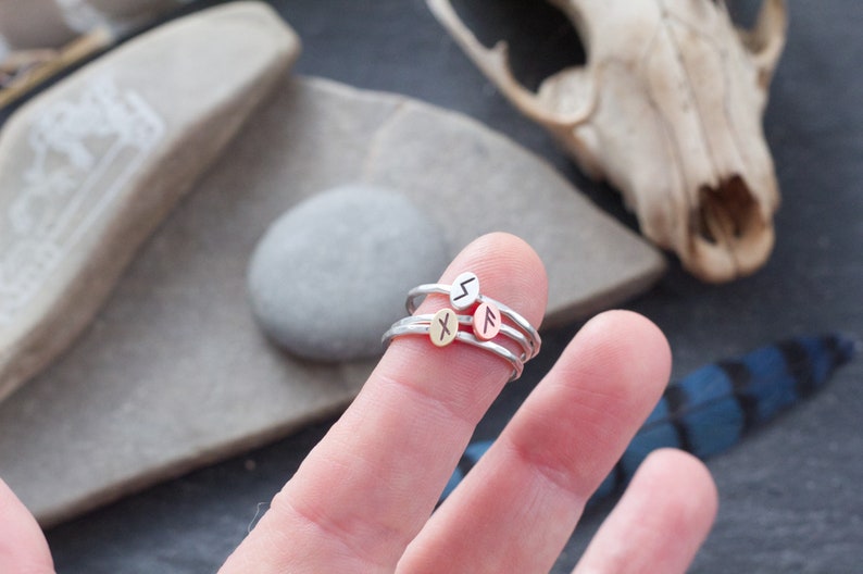 May include: Three silver rings with different runes engraved on them. The rings are stacked on a finger.