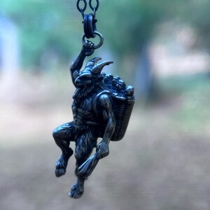 May include: A silver-toned pendant necklace featuring a mythological satyr figure. The satyr is depicted with horns, a beard, and a basket of grapes. The pendant is suspended from a delicate chain, showcasing intricate details and a rustic aesthetic.