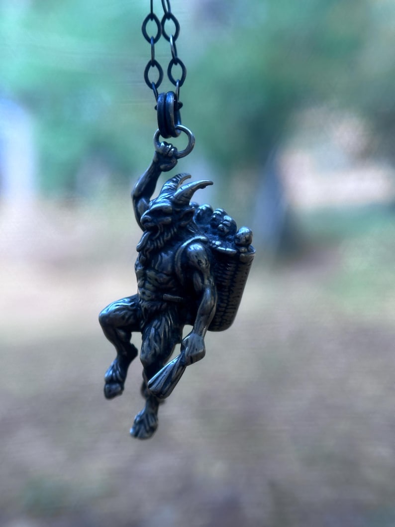 May include: A silver-toned pendant necklace featuring a mythological satyr figure. The satyr is depicted with horns, a beard, and a basket of grapes. The pendant is suspended from a delicate chain, showcasing intricate details and a rustic aesthetic.