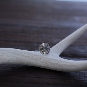 May include: A silver ring with a circular design featuring a stylized snowflake pattern. The ring is resting on a white antler.