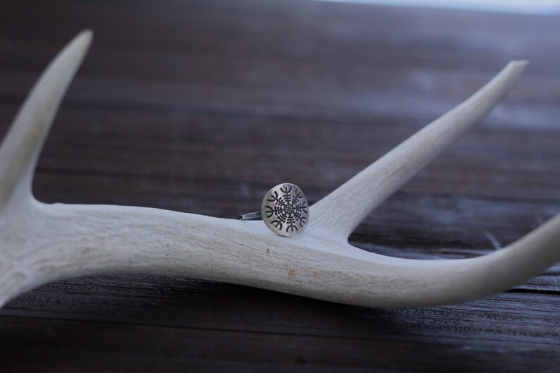 May include: A silver ring with a circular design featuring a stylized snowflake pattern. The ring is resting on a white antler.